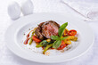 medallions of beef with grilled vegetables on a white plate on white table