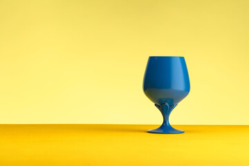 Blue wine glass on a yellow table against a yellow background.  Concept of minimalism. Place for text
