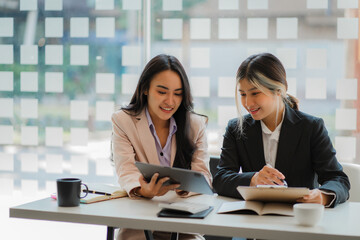 A meeting of two young Asian businesswomen to collaborate and work as a team for success in business and finance. Affiliate greetings and ideas with documents, graphs and a tablet on the table.