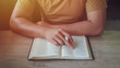 A man holding and read book on wood table with window light, crisis solution pray to God, Christian believe, trust and obey , morning devotional concept with copy space