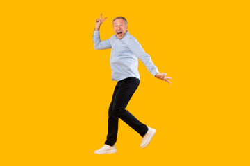 Wall Mural - Excited mature man jumping up at yellow orange studio