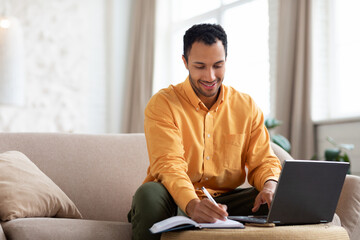 Portrait of smiling Arab man using laptop and writing