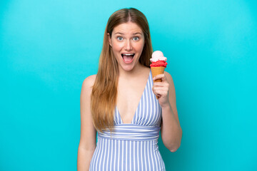 Young caucasian woman in swimsuit eating ice cream isolated on blue background with surprise and shocked facial expression