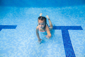 Wall Mural - Girl swimming underwater in the paddling pool. Diving. Learning child to swim. Enjoy swims and bubbles.