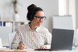© Prostock-studio - Portrait of happy young latin woman wearing wireless headphones watching online course, sitting at table
