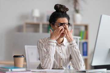 Poster - Female office worker in glasses rubbing tired eyes, exhausted from overworking, sitting at workplace in office