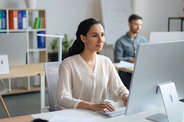 Canvas Print - Focused young woman working on computer at open space office with her male colleague