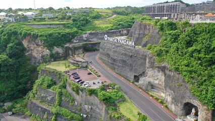 Wall Mural - Beautiful coastline beach with a white lighthouse, roads and tourist clubs on a sunny day. Aerial landscape of Pandawa Beach, Bali, Indonesia. Bird's-eye view of Ocean landscape.