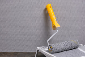 Wall Mural - Paint roller with yellow handle in tray for roller with gray paint on grey painted wall background.