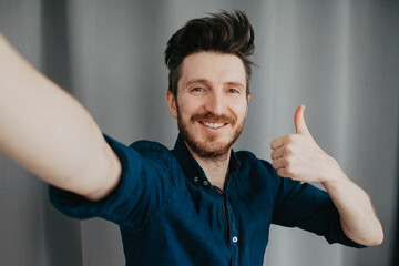 Handsome young man in a blue shirt by a grey background take a selfie. Smiling face. Place for text.