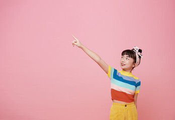 Canvas Print - smiling Asian girl pointing finger on blank space beside in pink isolated background.