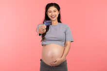 Asian Pregnant Woman Holding Credit Card Smile And Happiness Isolated On Pink Background.Cheerful Pregnancy Woman Enjoy With Credit Card To Shopping Baby Stuff.Pregnancy Prepare For Newborn Concept