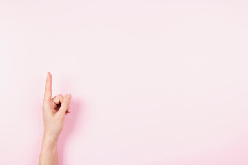 Wall Mural - Woman hand pointing up with index finger to something virtual and invisible, copy space on pastel pink background. Hand gesture, number one