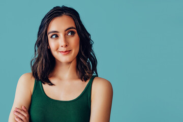 Brunette woman looking up to the side looking up wearing tank top on blue background studio portrait