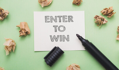 text Enter to win on a white note on a green background, a black marker lies next to it