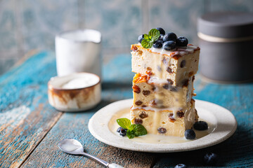 Wall Mural - Baked homemade cottage cheese casserole or pudding with raisins serving with blueberry and sour cream on blue background. Close-up.