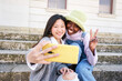 © CarlosBarquero - Smiling selfie of Two cheerful female friends having fun. Interracial Couple taking picture with smart mobile phone. Happy people enjoying vacations only for girls