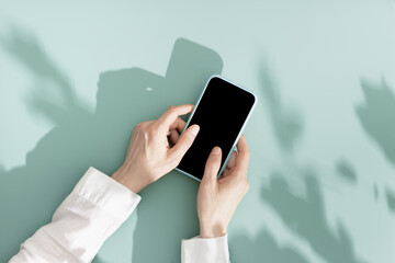 woman using phone with black blank screen, minimal flat lay on mint blue background. smartphone mock
