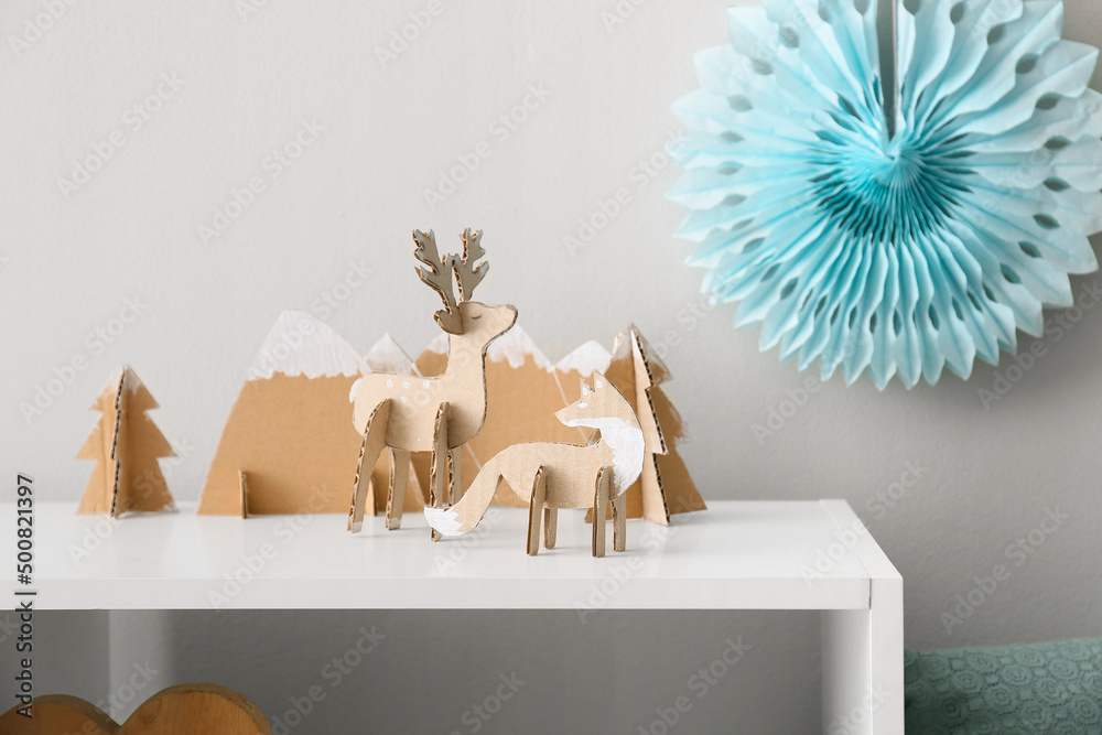 Different handmade cardboard toys on table near light wall