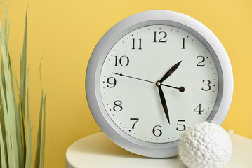 Table with new modern clock  and houseplant on color background, closeup