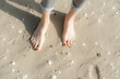 © Westend61 - Woman standing barefeet on sand with seashells at beach