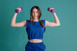 © Westend61 - Smiling young woman holding dumbbells flexing muscles against blue background
