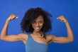 © Westend61 - Smiling woman flexing muscles against blue background