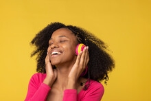 Happy Young Woman With Eyes Closed Enjoying Music Through Wireless Headphones Against Yellow Back Ground
