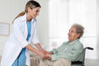 Young caregiver assisting senior woman in wheelchair indoors. Home health care service