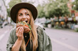 © Westend61 - Young woman with hat eating sandwich on street