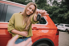 Happy Young Woman Handing Over Car Key To Friend On Parking Lot