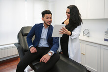 Smiling Doctor Discussing Over Digital Tablet With Patient At Aesthetic Clinic