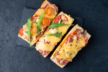 Wall Mural - Homemade pizza on a baguette on a dark table, top view.