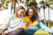 © Westend61 - Happy friends sharing mobile phone sitting in park on sunny day