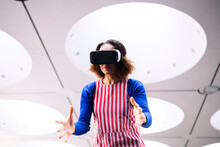 Mature Woman Wearing VR Goggles Gesturing Under Illuminated Ceiling