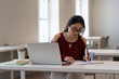 © DimaBerlin - Young student girl making homework in library. Asian female writing notes for educational project in university or college preparing for course work, test or graduation exam using laptop at campus