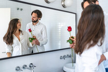 Man Presenting Woman With Red Rose In Front Of Mirror
