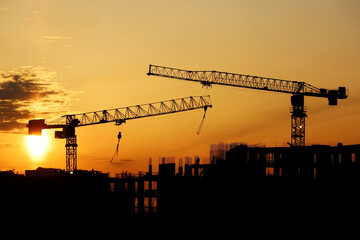 Wall Mural - Silhouettes of tower cranes and workers on scaffolding of unfinished building at sunrise. Housing construction, apartment block in city on dramatic sky background