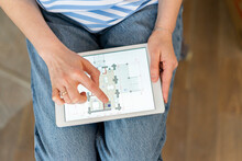 Hands Of Woman Holding Tablet PC Examining Blueprint Of Home