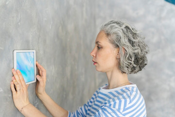 Woman with gray hair using tablet PC by gray wall