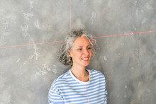 Smiling Woman With Laser Level On Face In Front Of Gray Wall