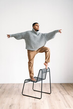 Man With Arms Outstretched Standing On Chair At Home
