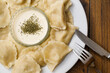 Polish dumplings on a white plate and serving of sour cream with herbs and fork and knife.