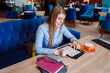 © Natalia - Young woman is working on her tablet in the cafe, cup of coffee next to her on the table.
