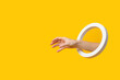 Hand with a round hole picks up an invisible object on a yellow background.