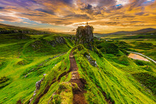 Sunset On The Isle Of Skye In Summer With Castle Ewen Rock And A Silhouette Of A Person At The Top. Landscape In Scotland In The Evening With Clouds In The Sky. Path On The Cliff Edge