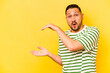© Asier - Young hispanic man isolated on yellow background shocked and amazed holding a copy space between hands.
