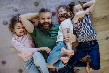 Wall Mural - Top view of cheerful father with three little daughters lying on floor together at home.