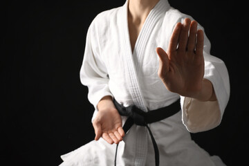 Man wearing keikogi and black belt on dark background, closeup. Martial arts uniform