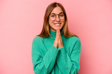 Young caucasian woman isolated on pink background holding hands in pray near mouth, feels confident.